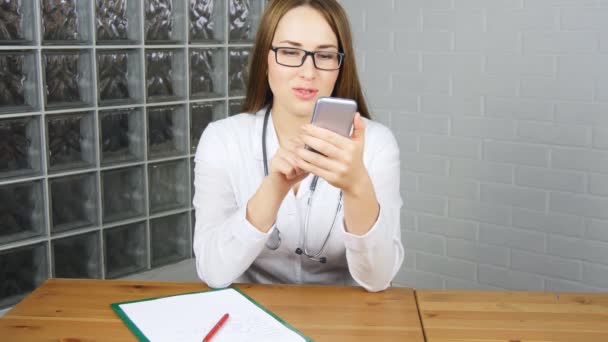 Femme médecin assis à son bureau et en utilisant un smartphone — Video