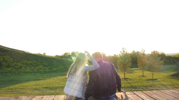 Vista trasera de la joven pareja feliz sentada al atardecer — Vídeos de Stock