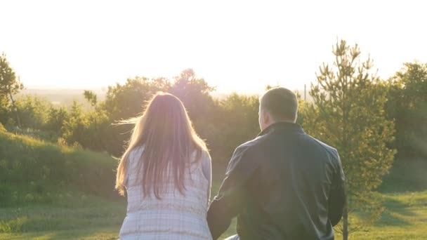Vue arrière du jeune couple heureux assis au coucher du soleil — Video