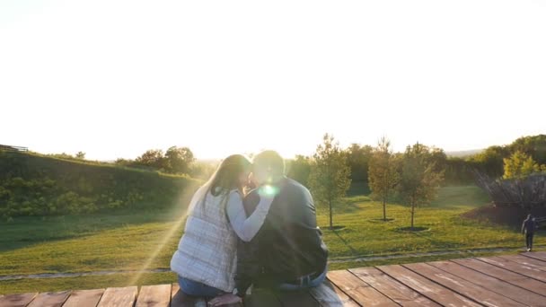 Vue arrière du jeune couple heureux assis au coucher du soleil — Video