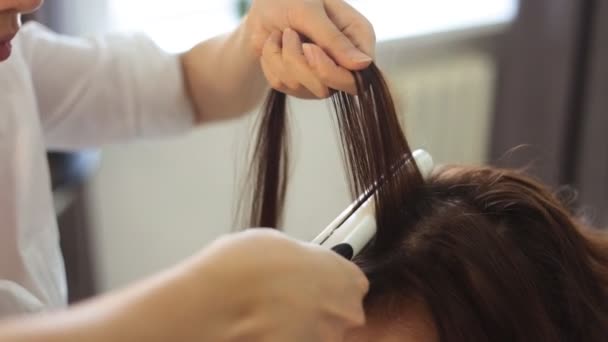 Mujer joven y peluquería con plancha para el cabello haciendo peinado en el salón de belleza — Vídeos de Stock