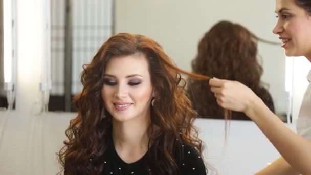 Mujer joven y peluquería con plancha para el cabello haciendo peinado en el salón de belleza — Vídeos de Stock