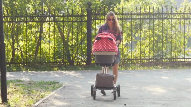 Mamma med bebis i barnvagn promenader i parken — Stockvideo