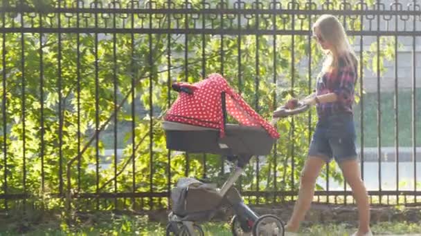 Mamma med bebis i barnvagn promenader i parken — Stockvideo