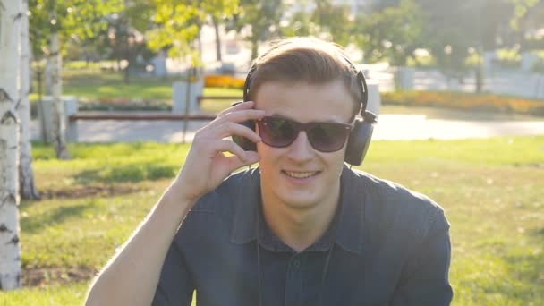 Hombre joven con auriculares en la hierba verde — Vídeo de stock