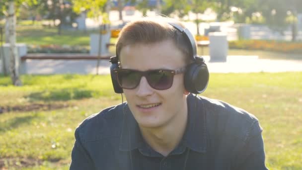 Hombre joven con auriculares en la hierba verde — Vídeo de stock