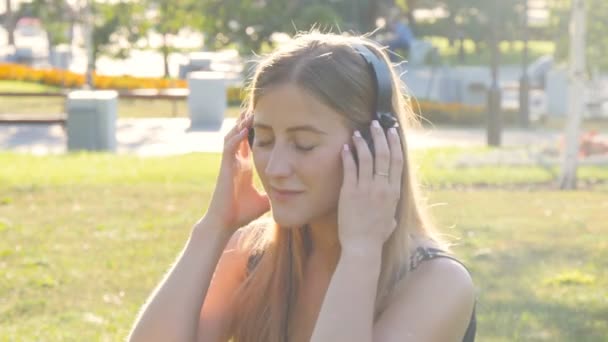 Joven hermosa mujer disfrutando de la música al aire libre en los auriculares — Vídeos de Stock