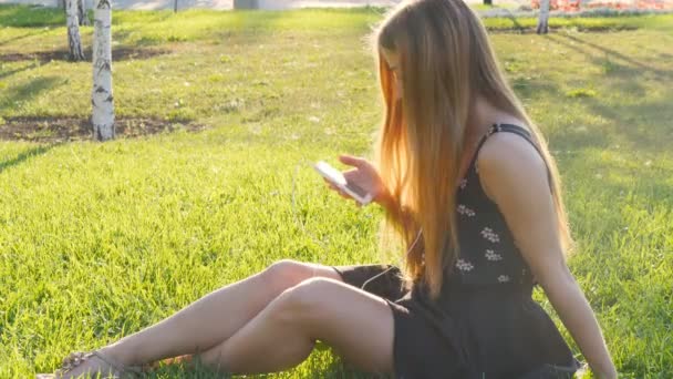 Mujer joven tocando el teléfono celular y acostado en el prado — Vídeos de Stock