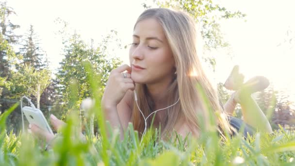 Mujer joven tocando el teléfono celular y acostado en el prado — Vídeos de Stock