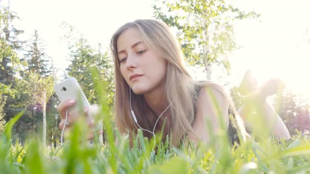 Mujer joven tocando el teléfono celular y acostado en el prado — Vídeos de Stock