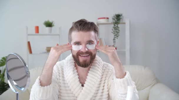 Tratamiento de la piel y concepto de autocuidado. Joven sonriente aplicando máscara ocular en casa — Vídeos de Stock