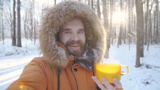 Vinterturism och vandring koncept. Ung skäggig man som tar selfie i skogen med en mugg varmt te i vinterskogen — Stockvideo