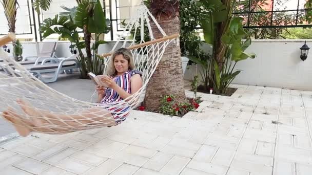 Señora leyendo el libro en la hamaca cerca de la piscina — Vídeo de stock