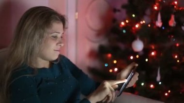 Genç kadın kanepede yalnız, Noel ağacı üzerinde oturan ve tablet kullanma