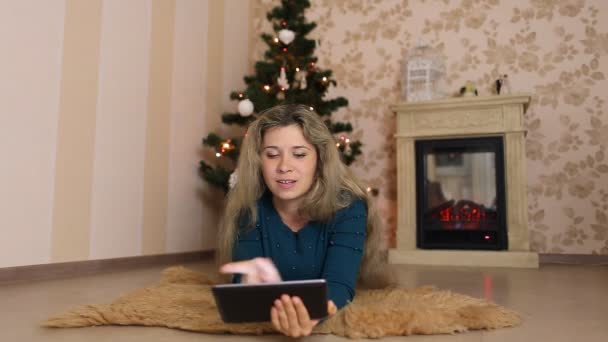 Молодая женщина сидит одна, перед рождественской елкой и использует столы — стоковое видео