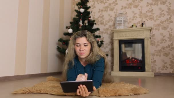 Молодая женщина сидит одна, перед рождественской елкой и использует столы — стоковое видео