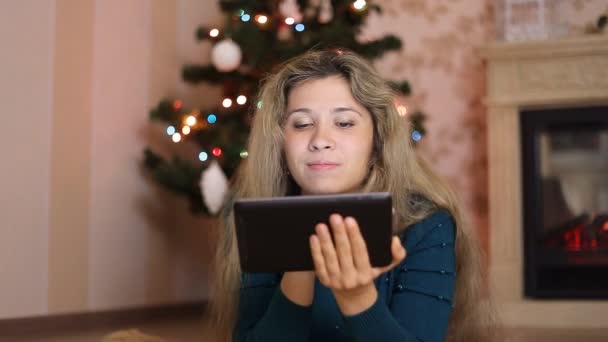 Jovem mulher sentada sozinha, na frente da árvore de natal e usando apresentado — Vídeo de Stock