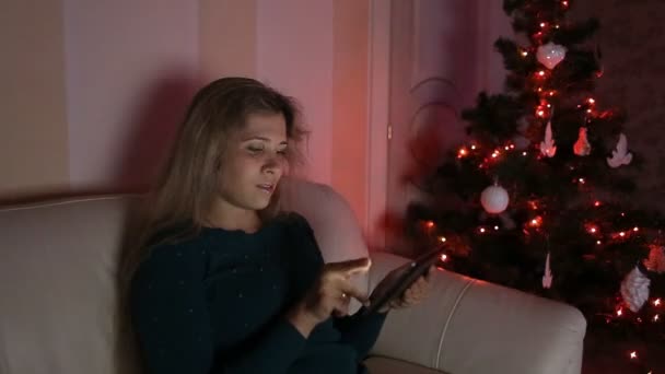 若い女性のクリスマス ツリーの上だけで、ソファに座って、タブレットを使用して — ストック動画