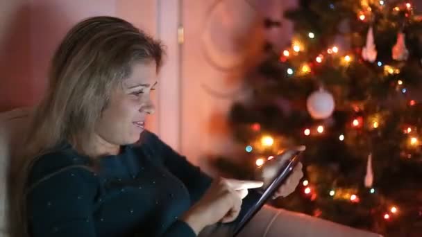 若い女性のクリスマス ツリーの上だけで、ソファに座って、タブレットを使用して — ストック動画