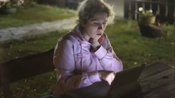Flicka med elektroniska tabletten satt på en bänk i parken — Stockvideo