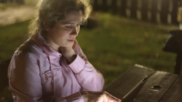 Menina com o tablet eletrônico sentado em um banco no parque — Vídeo de Stock