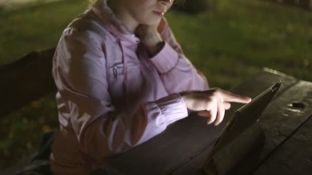 Fille avec la tablette électronique assis sur un banc dans le parc — Video