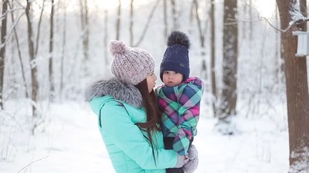 Счастливая мать держит маленькую девочку на прогулке по зимнему заснеженному лесу — стоковое видео