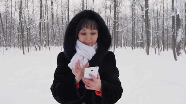 Mujer joven sonriendo con teléfono inteligente y paisaje de invierno en cámara lenta — Vídeos de Stock