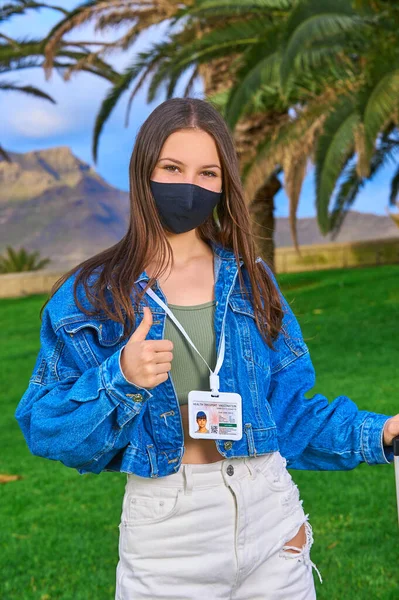 Halka açık bir yerde Palm Park 'ın arka planında genç bir kız. Aşı pasaportlu maskeli bir kadın. Yeni normal seyahat kavramı.