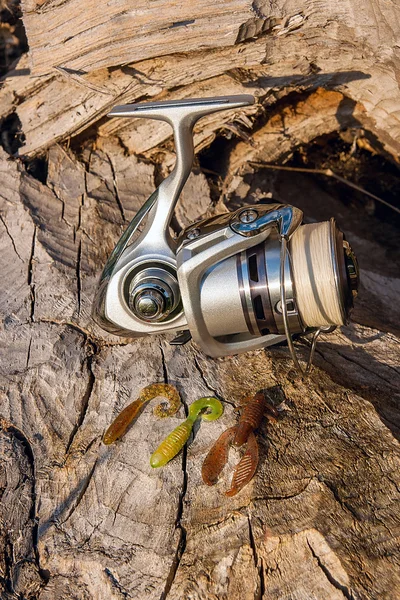 Fishing reel and various kind of silicon baits on the natural ba — Stock Photo, Image