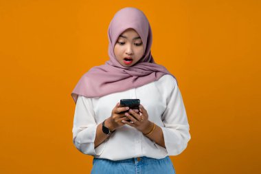 Sarı arka planda cep telefonu kullanan Asyalı genç bir kadın şok oldu.