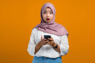 Sarı arka planda cep telefonu kullanan Asyalı genç bir kadın şok oldu.