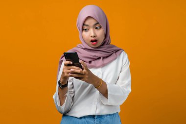 Sarı arka planda cep telefonu kullanan Asyalı genç bir kadın şok oldu.