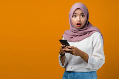 Sarı arka planda cep telefonu kullanan Asyalı genç bir kadın şok oldu.