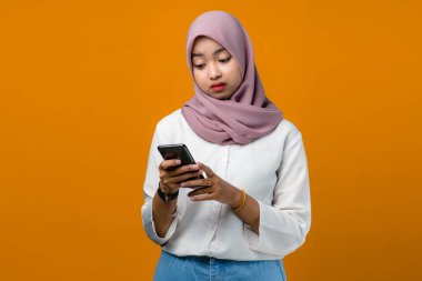 Üzgün genç Asyalı kadın sarı arka planda cep telefonu kullanıyor.