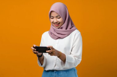 Gülümseyen Asyalı kadın sarı arka planda akıllı telefon kullanıyor.