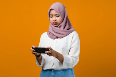 Sarı arka planda akıllı telefon kullanan kafası karışmış genç Asyalı kadın.