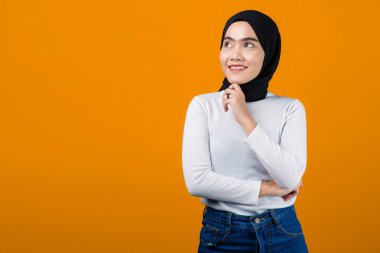 Genç Asyalı kadın düşünüyor ve tesettürlü mutlu görünüyor.