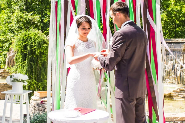 Brudgummen ger en förlovningsring till sin brud under bågen. Bröllop och smekmånad koncept. — Stockfoto