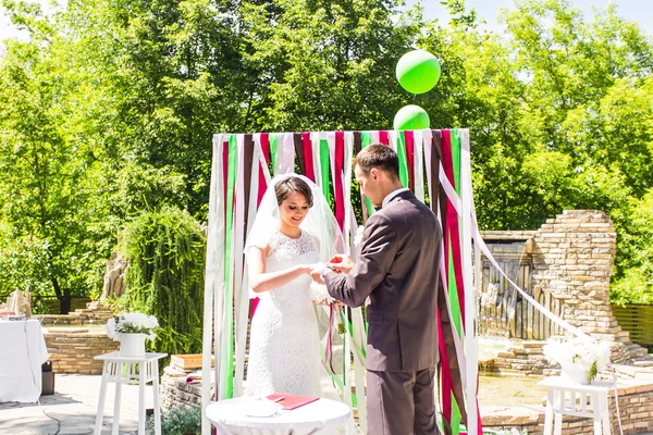 Der Bräutigam schenkt seiner Braut unter dem Bogen einen Verlobungsring. Hochzeits- und Flitterwochenkonzept. — Stockfoto