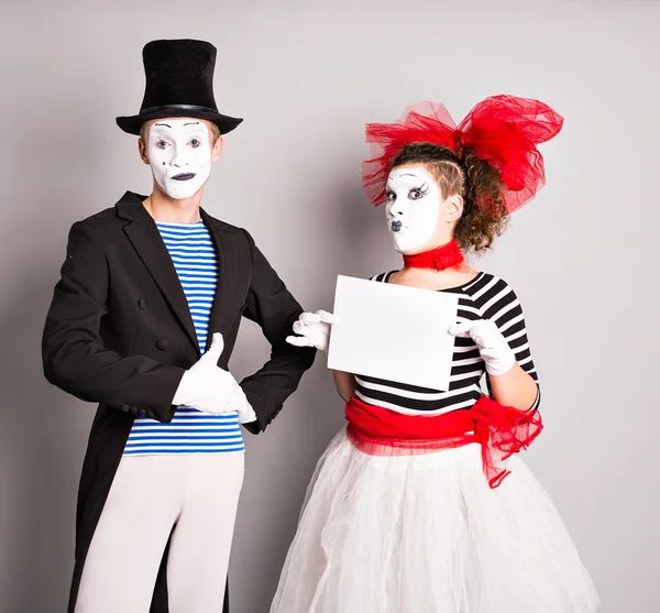 Portrait of happy smiling young actors showing blank signboard, with copyspace area for text or slogan, against grey background — Stock Photo, Image