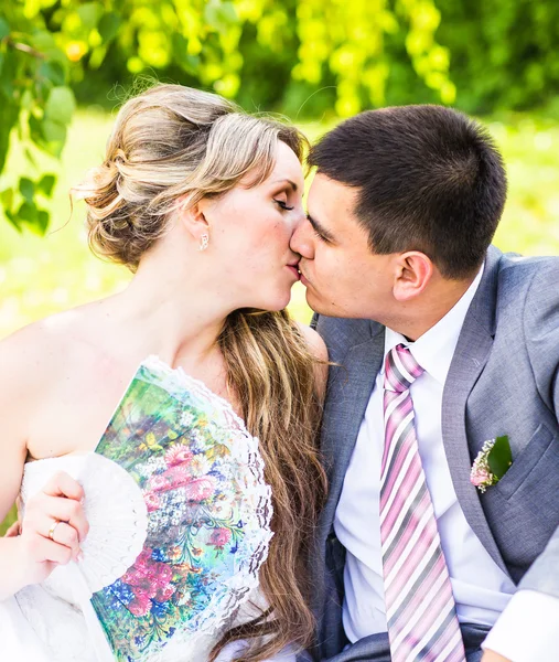 美しい花嫁と花婿の草の中に座って、キスします。若い結婚式のカップル — ストック写真