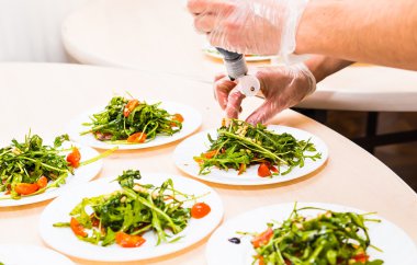 Process of preparing sauce for salad, at kitchen. Man pouring sauce into plate with salad ingredients
