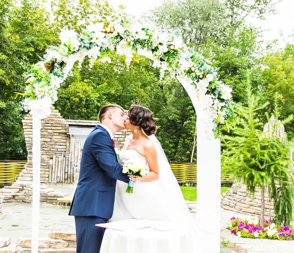 Primeiro beijo de casal recém-casado sob arco de casamento — Fotografia de Stock