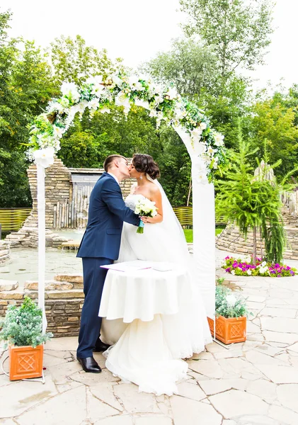 Primeiro beijo de casal recém-casado sob arco de casamento — Fotografia de Stock