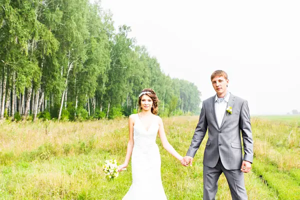 Jovem casal apaixonado noiva e noivo posando em um campo com grama amarela em seu dia do casamento no verão — Fotografia de Stock