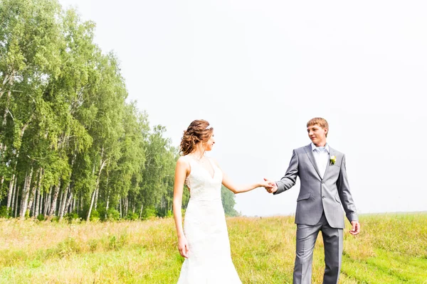 Jeune couple amoureux mariée et marié posant dans un champ avec de l'herbe jaune dans leur jour de mariage en été — Photo