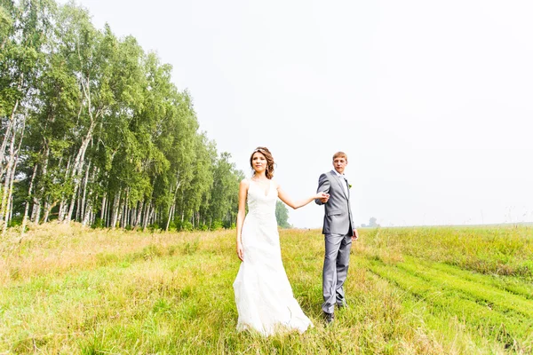 Jovem casal apaixonado noiva e noivo posando em um campo com grama amarela em seu dia do casamento no verão — Fotografia de Stock