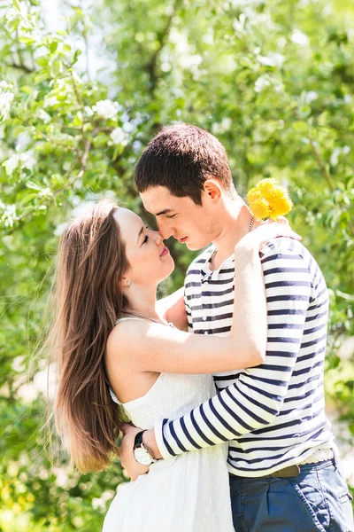 Pareja cariñosa bajo ramas florecientes día de primavera. Joven morena adulta hombre y mujer besándose en flor fresca jardín de manzanos o cerezos. dulce beso — Foto de Stock