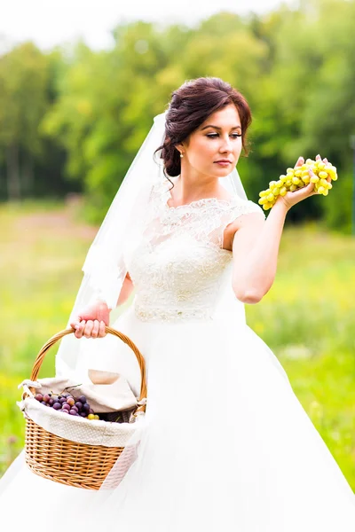 Outside portrait of beautiful young bride with grapes in a park — Stock Photo, Image